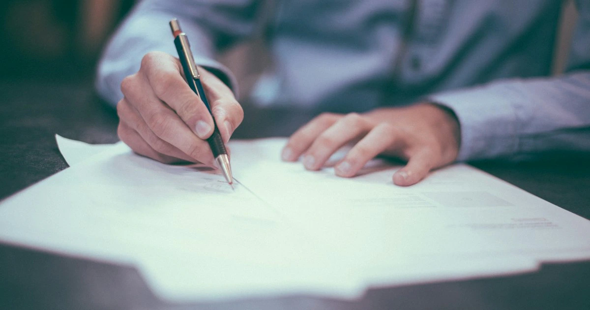 Persona firmando un documento oficial con bolígrafo sobre un escritorio